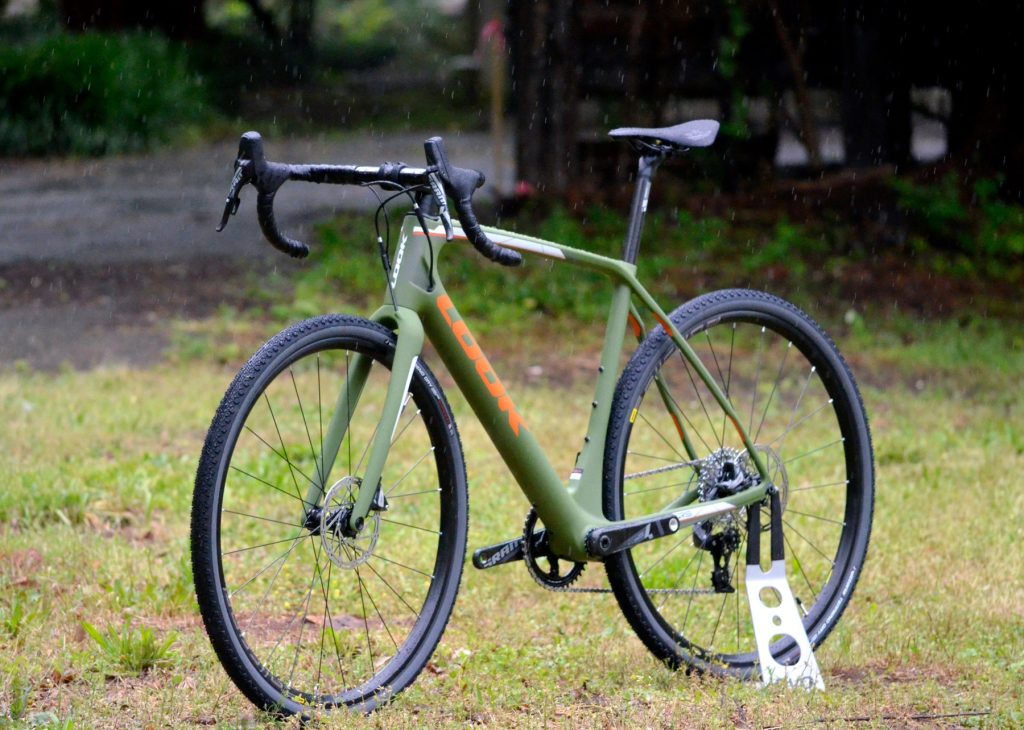 Green drop-bar gravel bicycle with disc brakes and wide tires standing on grass.