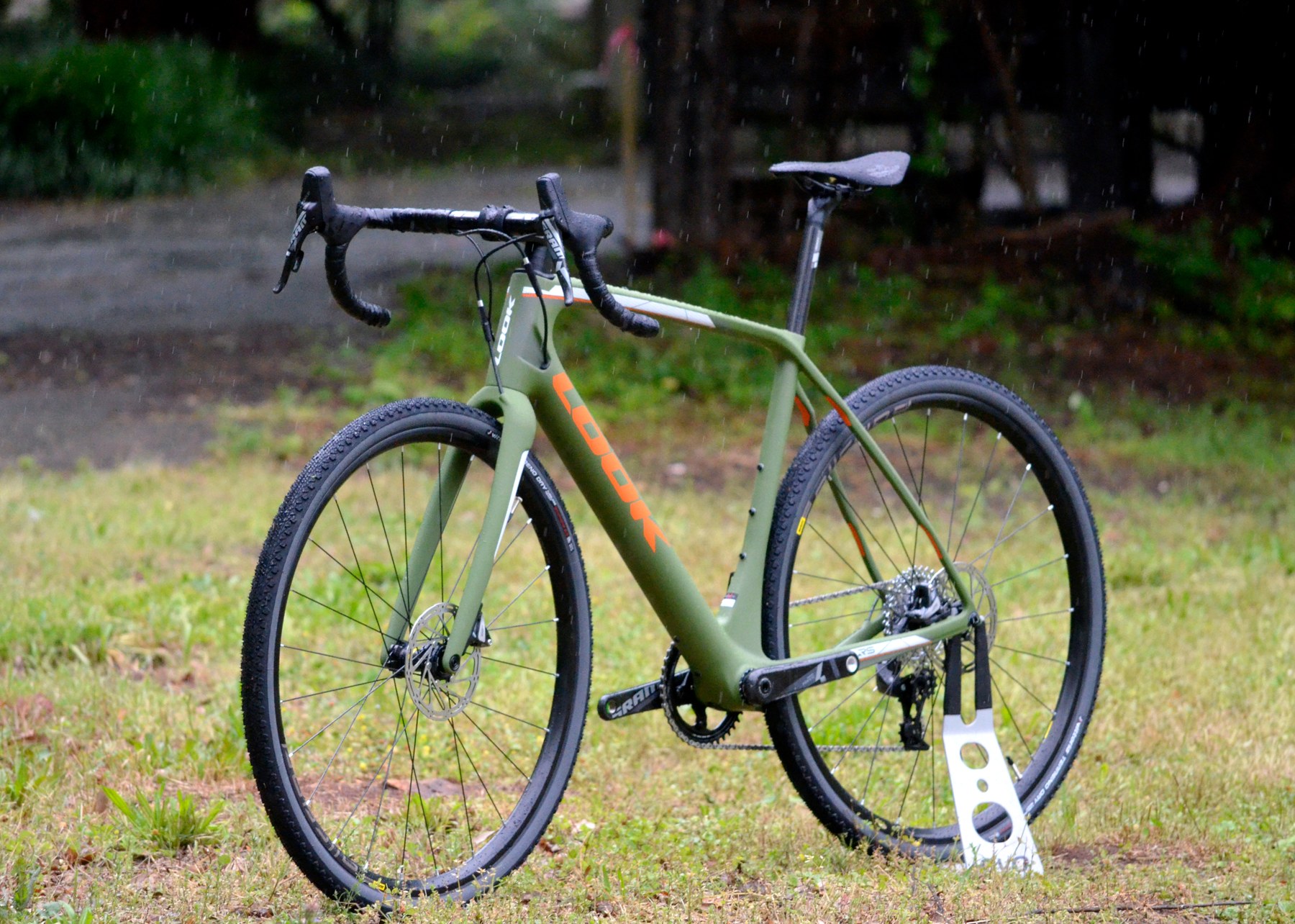 Green drop-bar gravel bicycle with disc brakes and wide tires standing on grass.