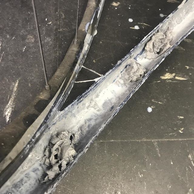 Pale sealant residue and clumps inside a removed tubeless bicycle tire beside its wheel.