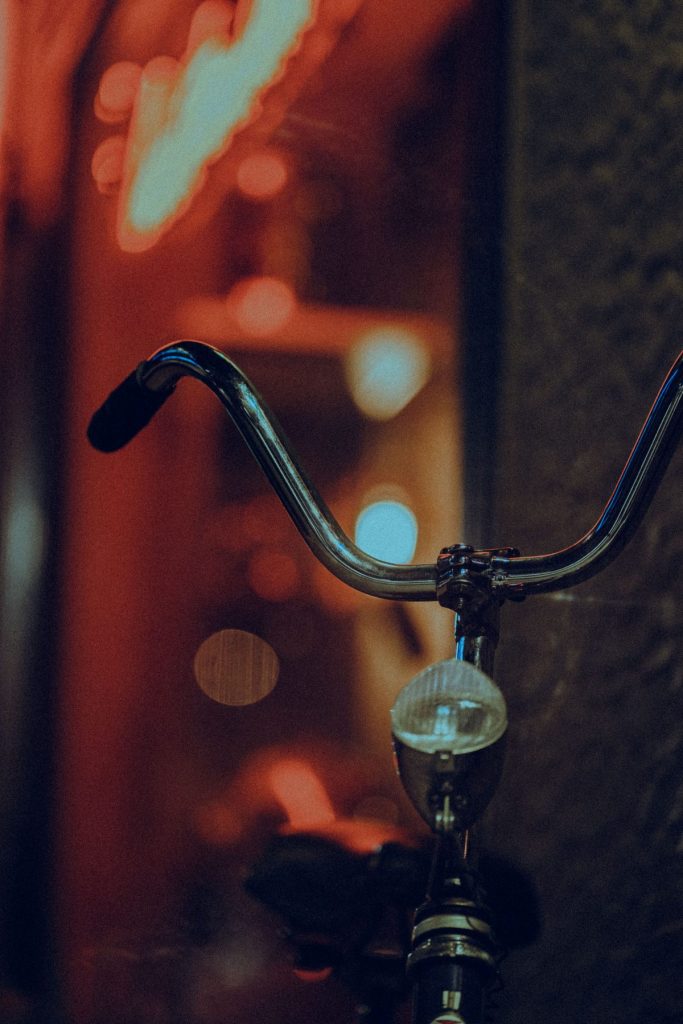 Small front light mounted below chrome bicycle handlebars against a blurred night street.
