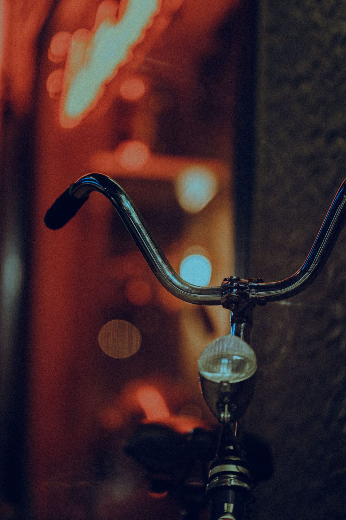 Small front light mounted below chrome bicycle handlebars against a blurred night street.