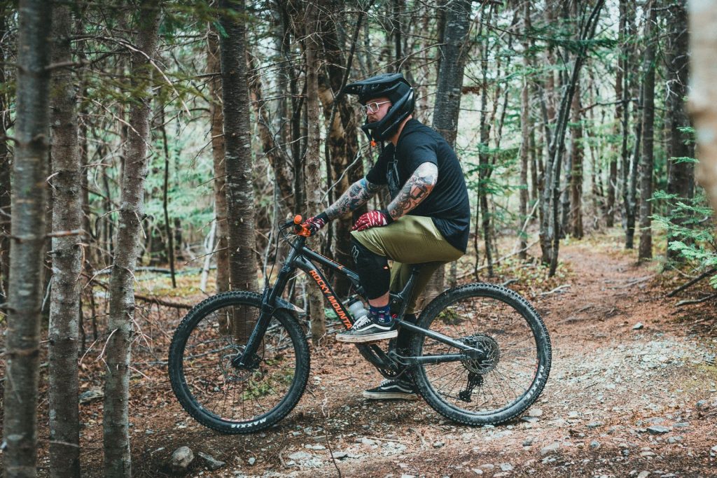 Mountain biker in a black helmet riding a dirt trail through a pine forest.