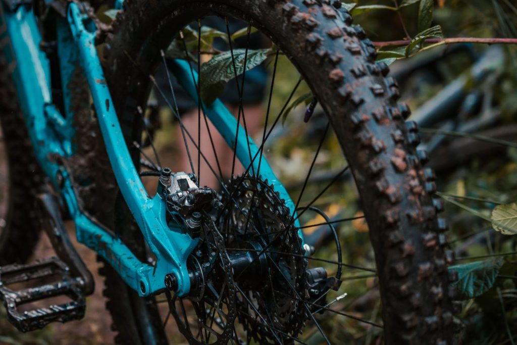 Muddy knobby rear tire and drivetrain on a blue mountain bike in wet conditions.