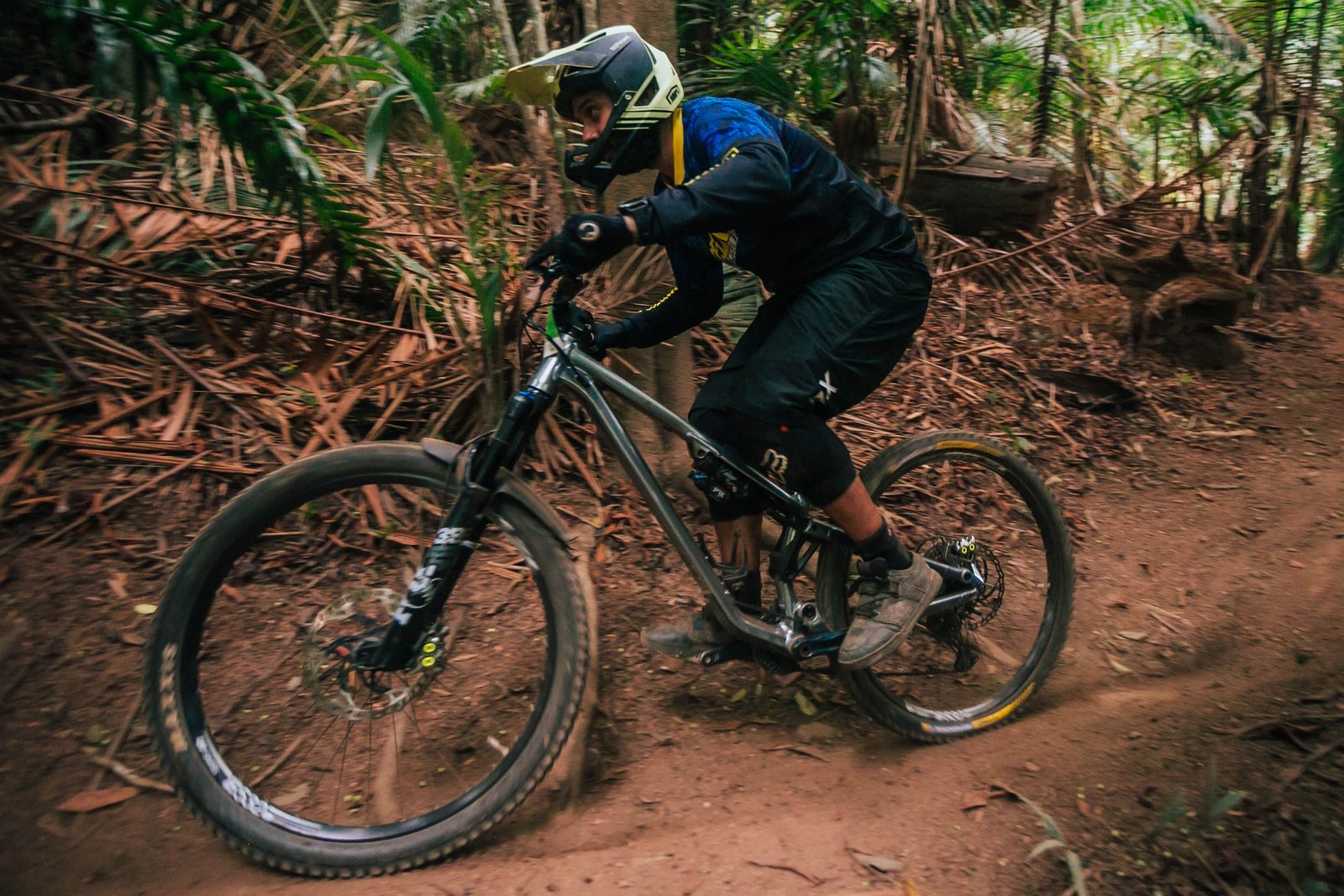 Mountain biker in a helmet and protective gear riding a dirt trail through a forest.
